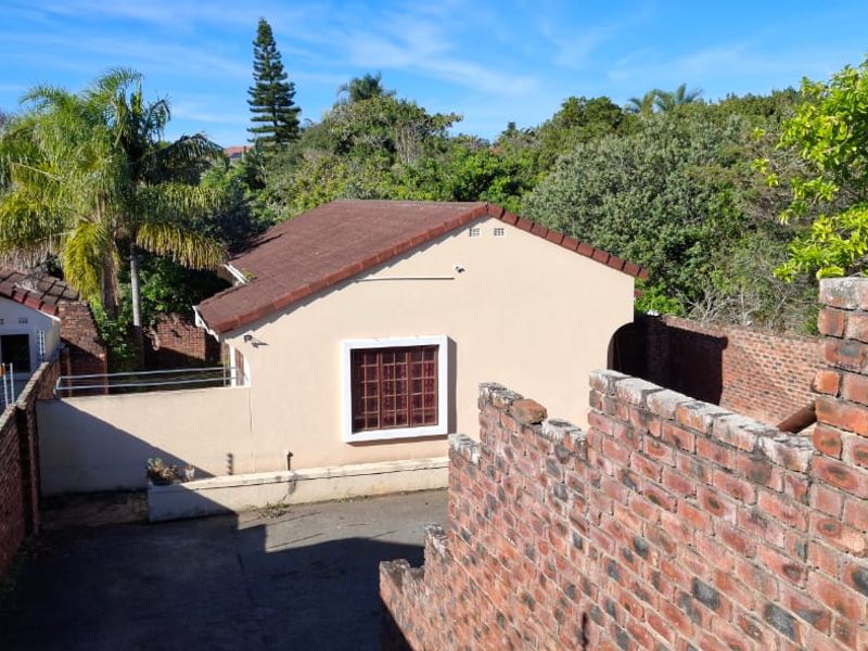 An elevated view of the rear exterior showing a detached structure, paved driveway, and brick boundary walls with electric fencing.