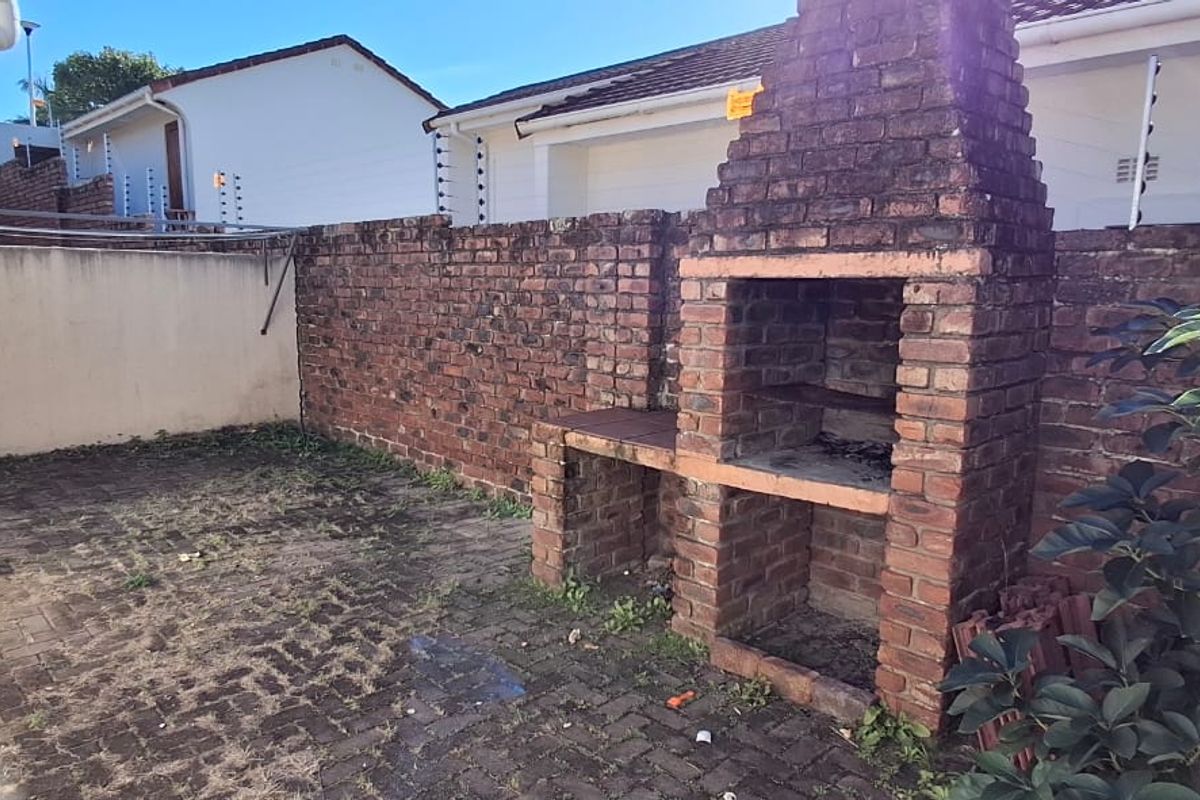 Rear courtyard featuring a built-in brick braai, paved flooring, and secure boundary walls with electric fencing.