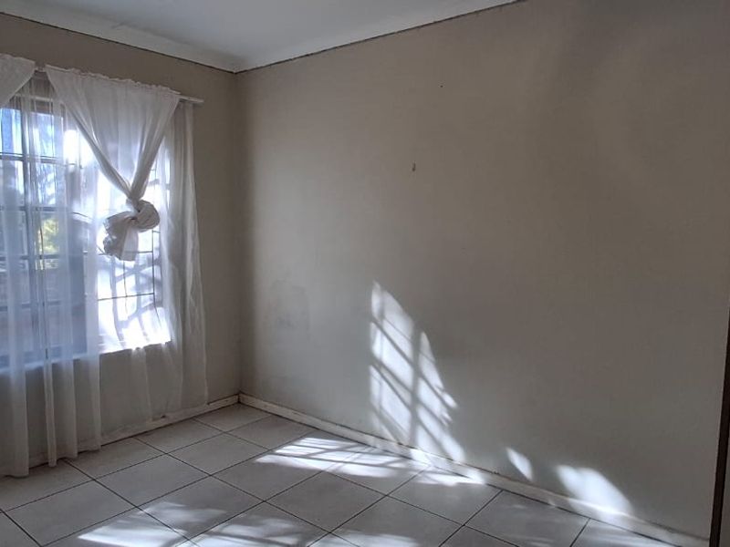 An empty bedroom featuring tiled flooring and a window with security bars, offering a blank canvas for potential interior updates.
