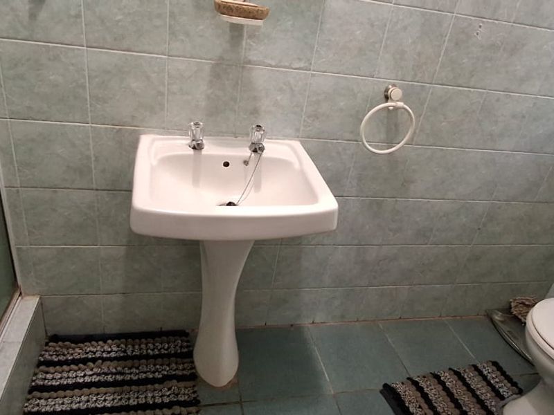 A functional bathroom featuring a pedestal basin, toilet, and shower enclosure with dated ceramic wall and floor tiling.