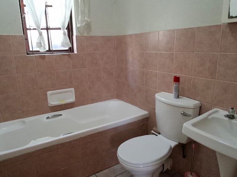 A dated bathroom featuring a standard bathtub, pedestal basin, and toilet with original pink wall tiling throughout.