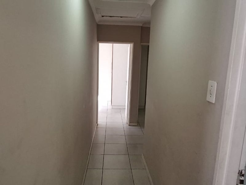 A narrow interior hallway featuring tiled flooring and a built-in cupboard, showing signs of wear on the walls and ceiling.