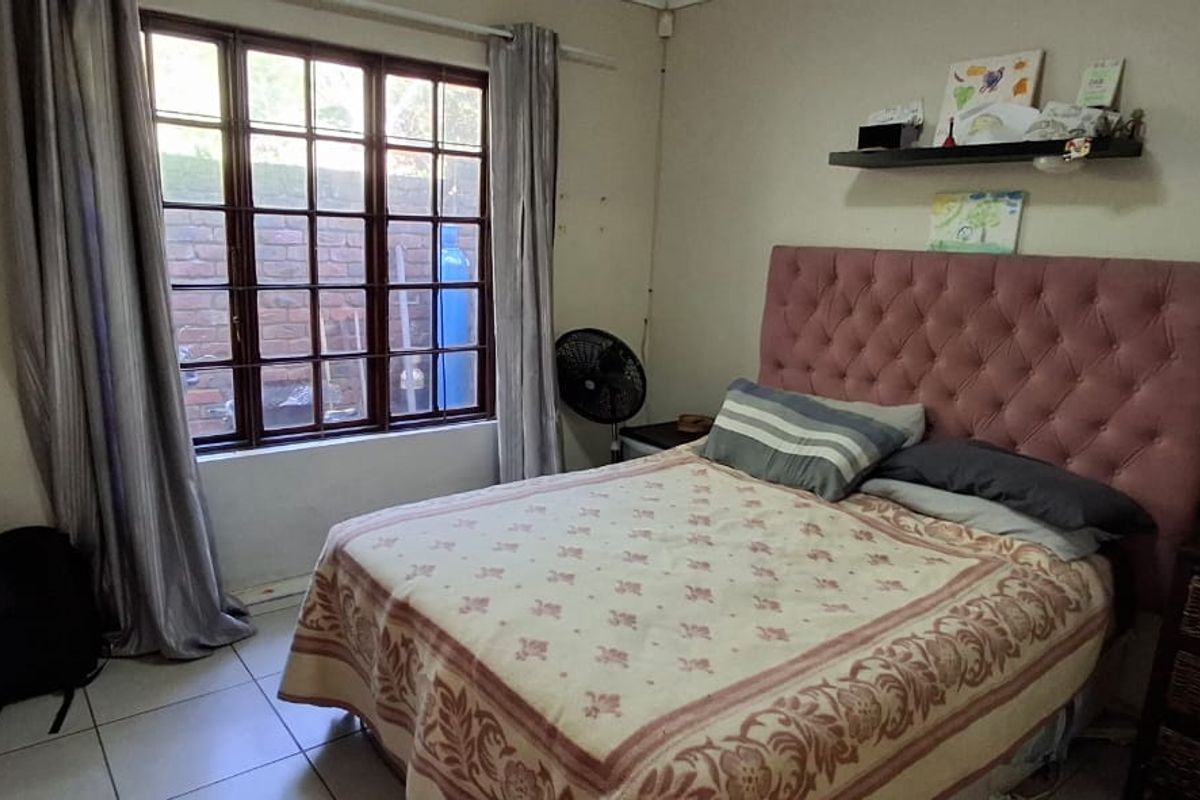 A functional bedroom featuring tiled flooring and a large timber-framed window, providing natural light and a view of the exterior brick wall.