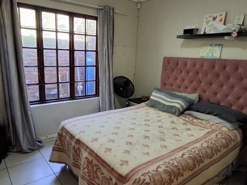 A functional bedroom featuring tiled flooring and a large timber-framed window, providing natural light and a view of the exterior brick wall.
