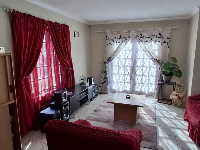 A living room featuring tiled flooring, a large window with red curtains, and french doors leading to the exterior.
