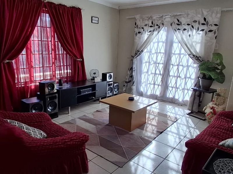A living room featuring tiled flooring, a large window with security bars, and a sliding glass door providing access to the exterior.