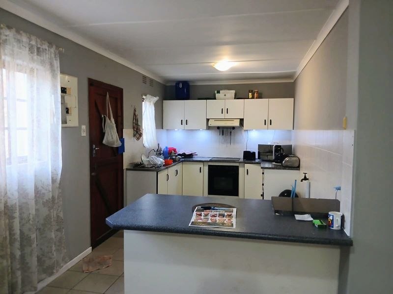 Functional kitchen featuring white cabinetry, dark laminate countertops, built-in oven and hob, and a convenient breakfast bar for casual dining.