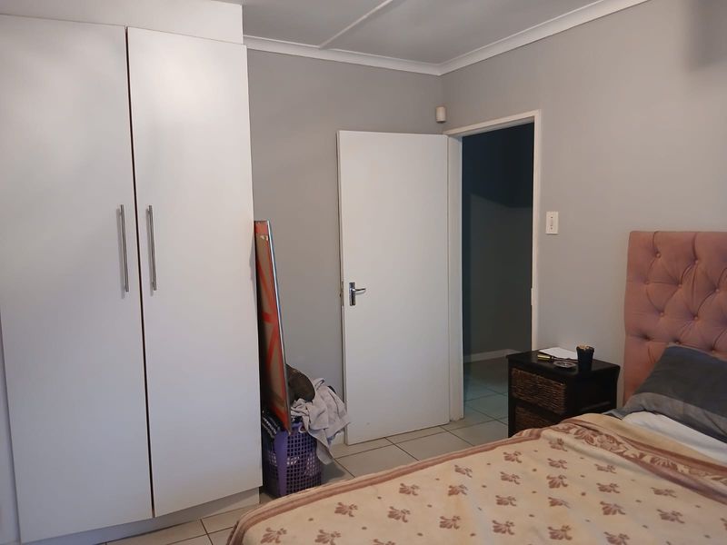 A bedroom featuring neutral grey walls, tiled flooring, and a white built-in wardrobe with modern handles.