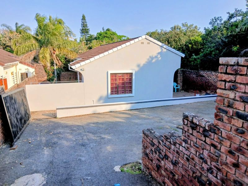 Exterior view of a residential property featuring a tiled roof, plastered facade, and a paved driveway enclosed by brick boundary walls.
