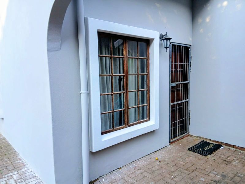 A view of the rear exterior featuring a timber-framed window, a secure metal gate, and a paved patio area.