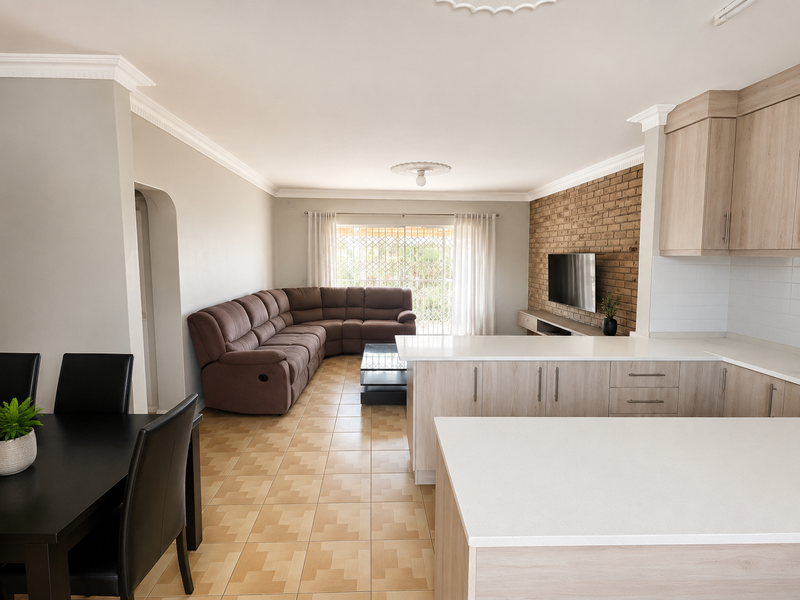 Open-plan living and kitchen area featuring a brick feature wall, modern cabinetry with quartz countertops, and neutral ceramic floor tiles.