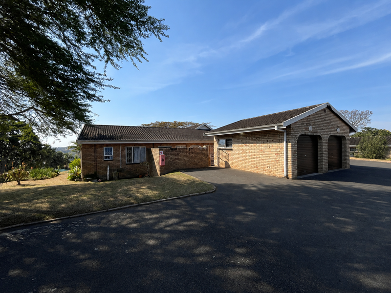Front exterior view of a townhouse featuring a double garage, brick facade, tiled roof, and an asphalt driveway with surrounding landscaped garden area.