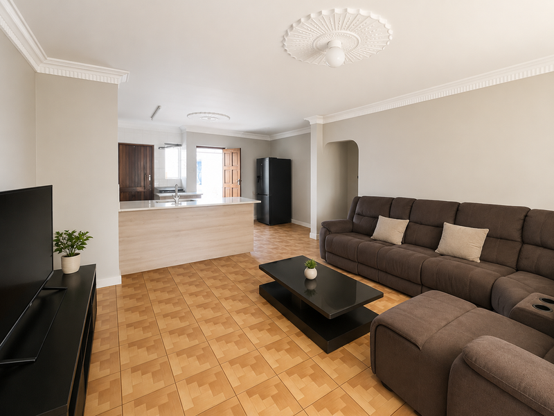 Open-plan living area featuring tiled flooring, decorative crown molding, ceiling roses, and a functional kitchen island with a breakfast counter.