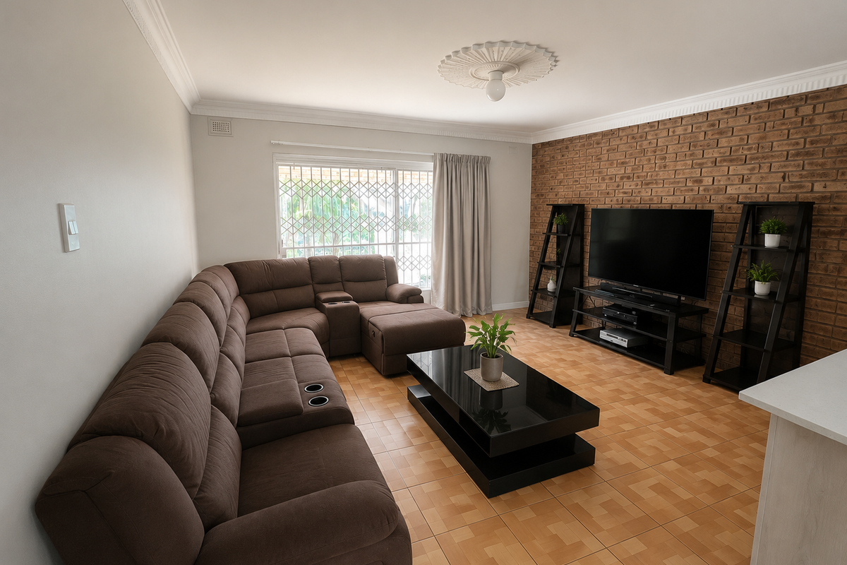 A comfortable living room featuring an exposed brick accent wall, ceramic floor tiles, and a decorative ceiling rose, providing a warm and inviting atmosphere.