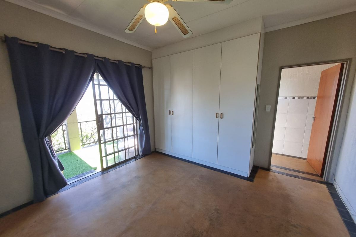 A spacious bedroom featuring built-in cupboards, a ceiling fan, and a sliding glass door providing access to an outdoor balcony area.