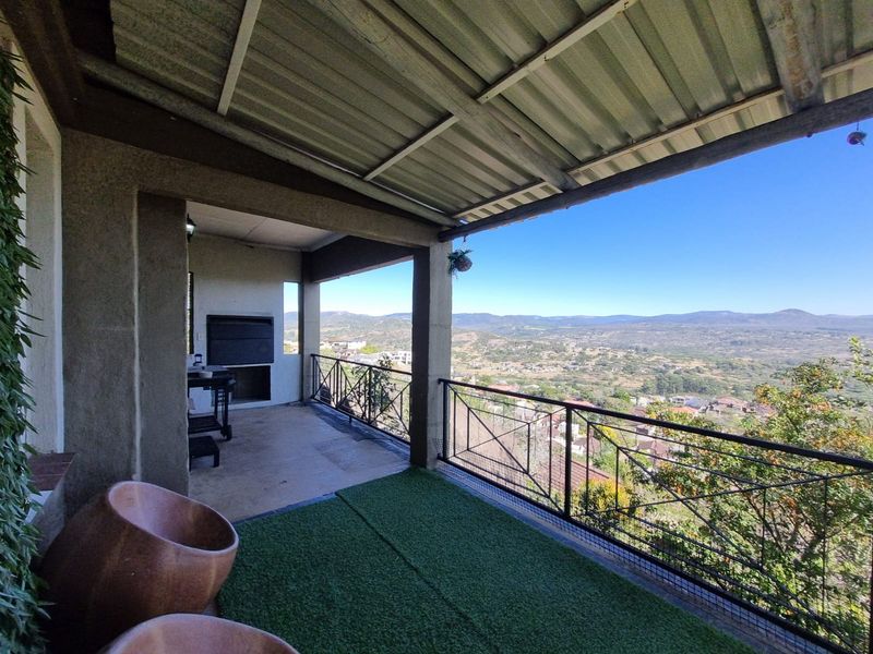 Covered balcony featuring a built-in braai, metal balustrade, and expansive elevated views over the surrounding landscape.