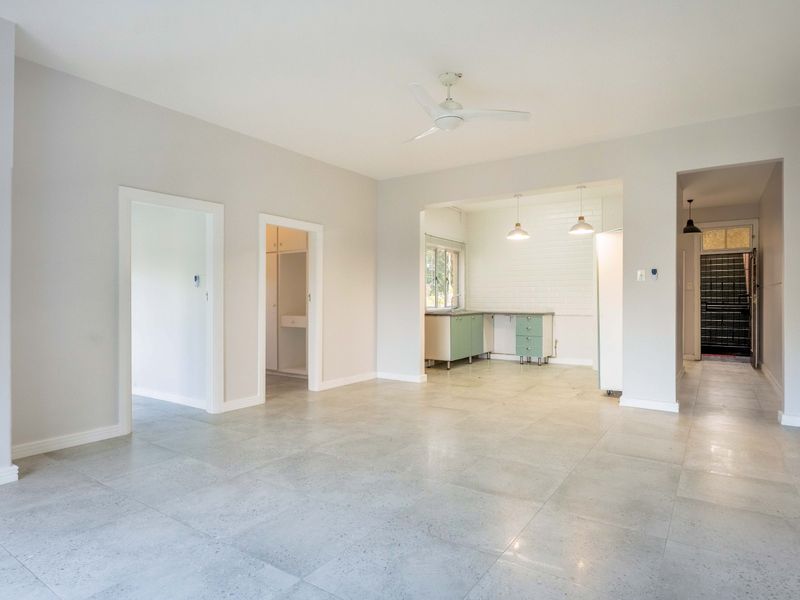 Spacious open-plan living area featuring neutral tones, tiled flooring, a ceiling fan, and an adjoining kitchen space with built-in cabinetry.