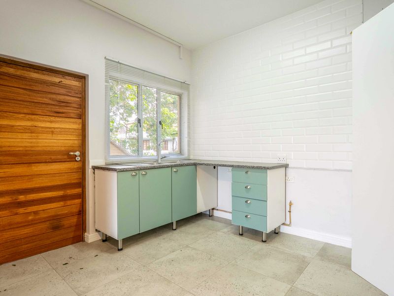 A functional laundry area featuring built-in cabinetry, a stainless steel sink, tiled flooring, and a timber door, offering a clean and practical utility space.