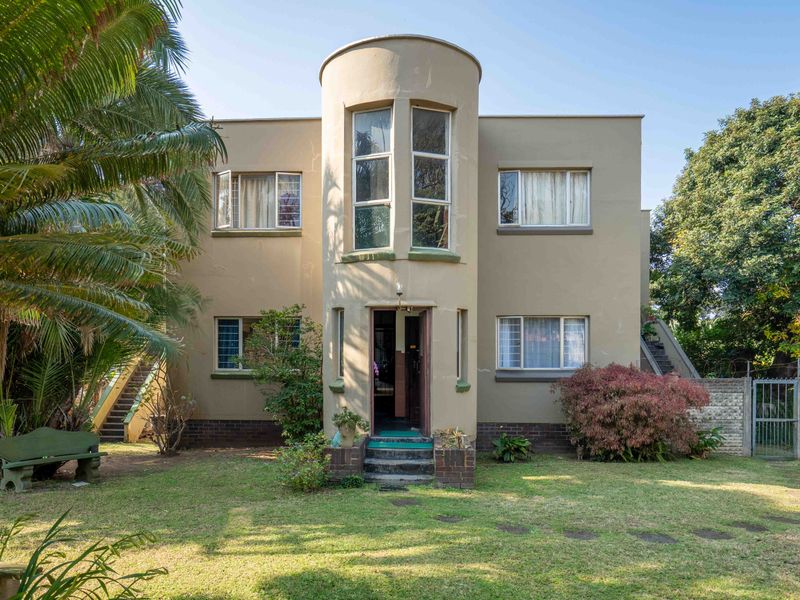 Front elevation of a two-story townhouse featuring a central curved architectural detail, large windows, and a front garden with a paved entrance.