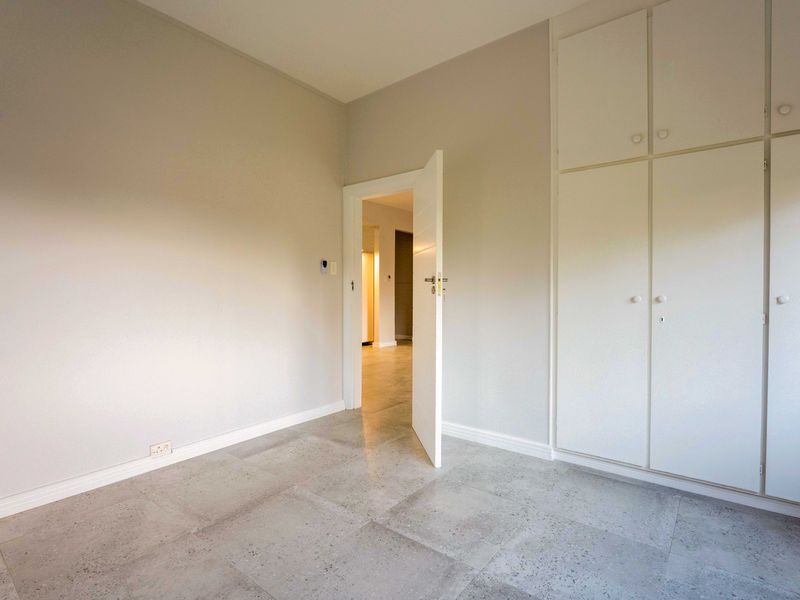 A clean, empty bedroom featuring neutral wall tones, modern grey tiled flooring, and ample built-in cupboard storage space.