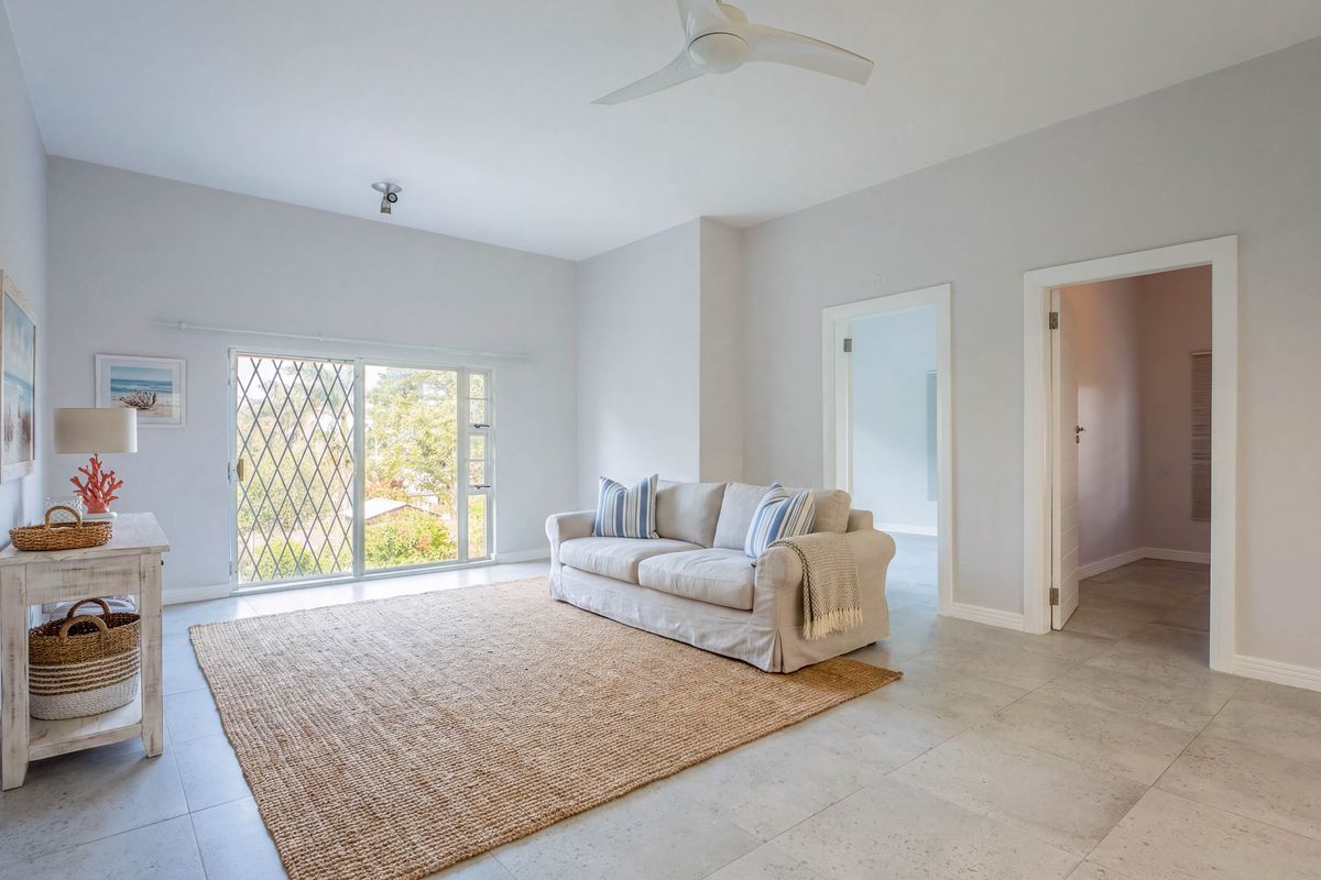 Bright living room featuring neutral tiled flooring, a ceiling fan, and a sliding glass door with security gate providing access to the exterior.