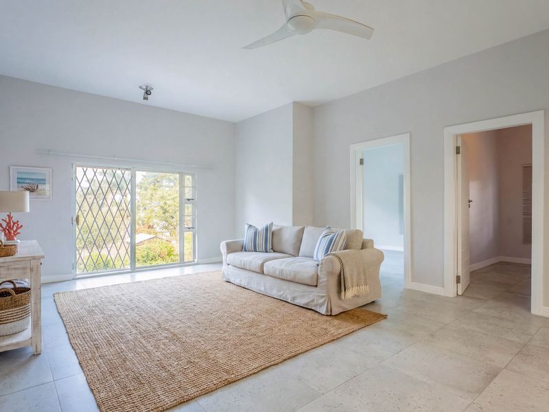 Bright living room featuring neutral tiled flooring, a ceiling fan, and a sliding glass door with security gate providing access to the exterior.