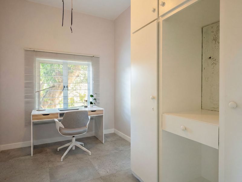A functional bedroom featuring tiled flooring, a built-in wardrobe with internal wear, and a window with venetian blinds, suitable for use as a home office.