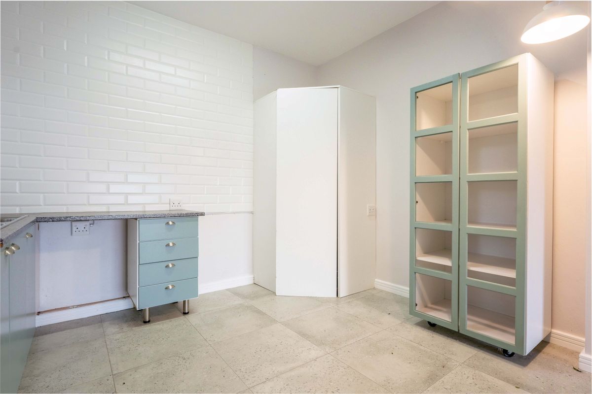 A clean, modern kitchen area featuring light blue cabinetry, stone countertops, a white brick-style splashback, and neutral tiled flooring.