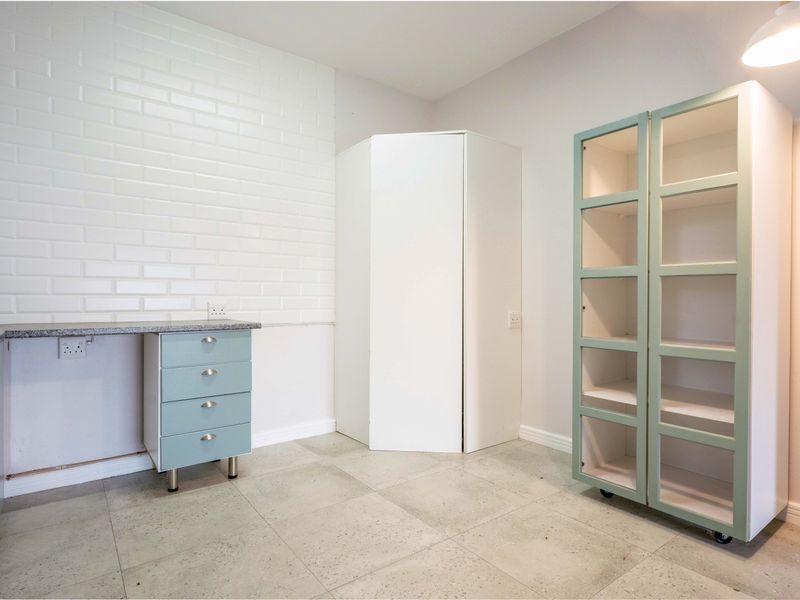 A clean, modern kitchen area featuring light blue cabinetry, stone countertops, a white brick-style splashback, and neutral tiled flooring.