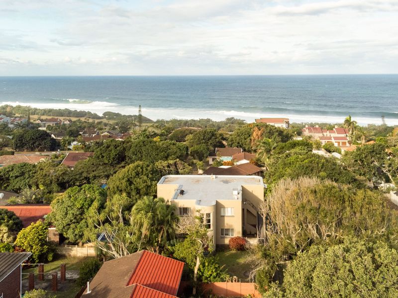 An aerial view of the townhouse property, showcasing its location within a lush, green coastal neighborhood with proximity to the ocean.