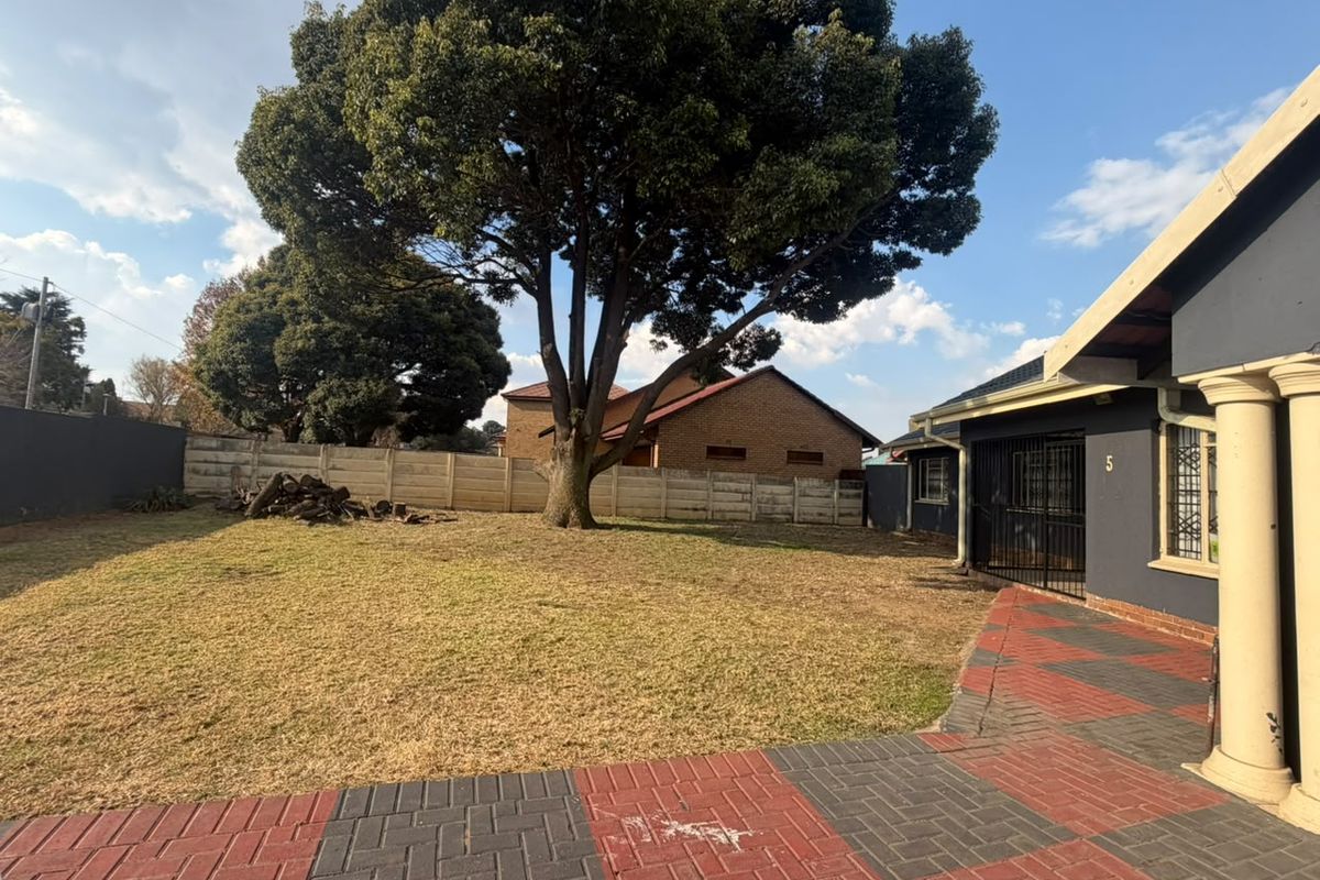 A spacious rear garden featuring a large mature tree, precast concrete boundary wall, and a paved patio area with decorative columns.