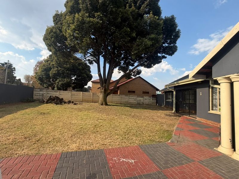 A spacious rear garden featuring a large mature tree, precast concrete boundary wall, and a paved patio area with decorative columns.