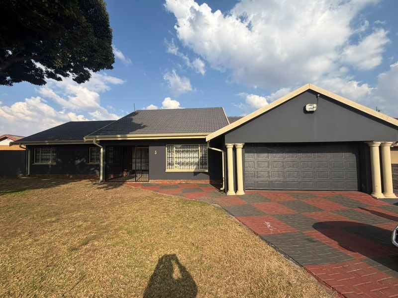 Front elevation of a single-story house featuring a dark grey facade, tiled roof, double garage, and a patterned paved driveway.