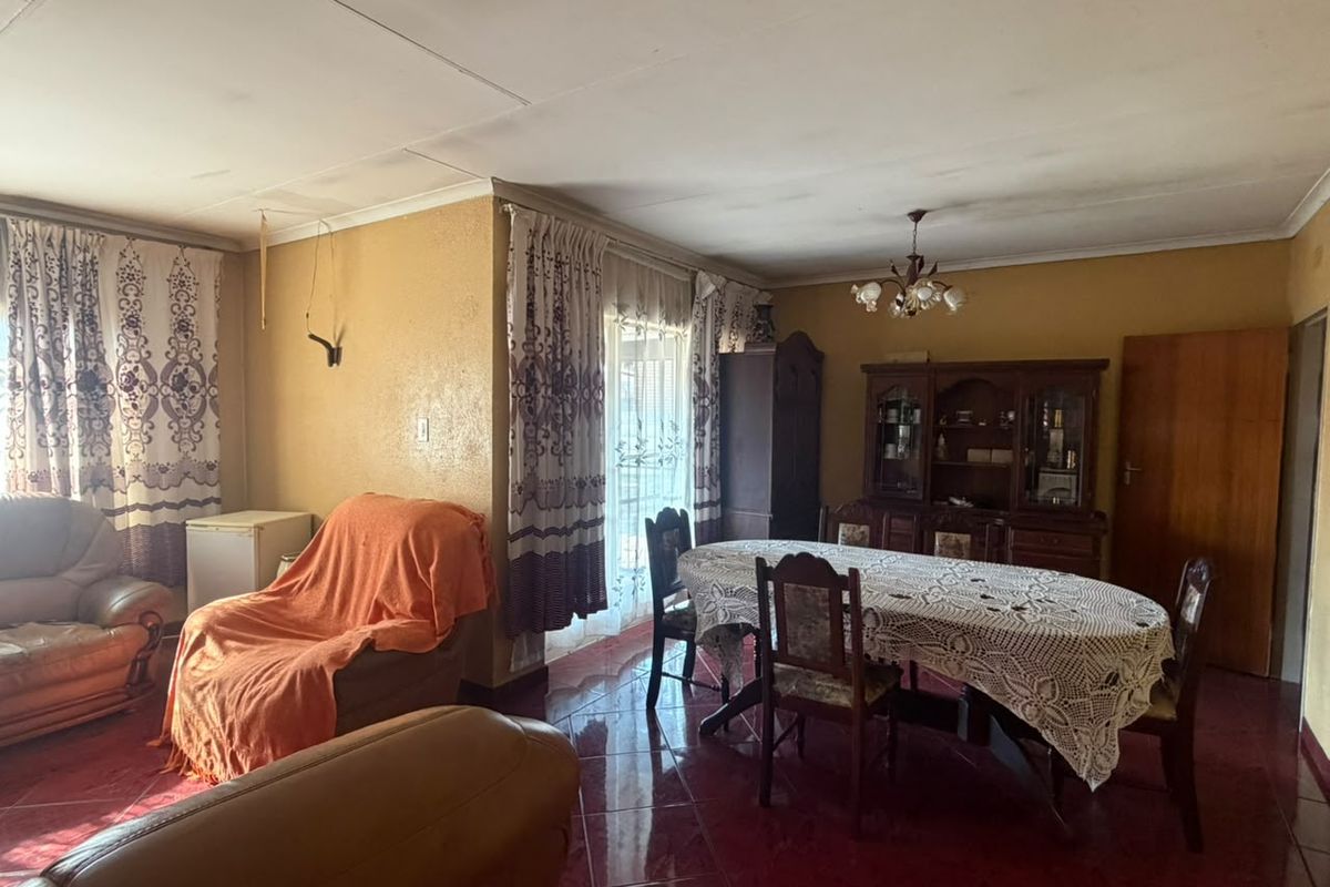 Spacious living and dining area featuring tiled flooring and a central chandelier, requiring cosmetic updates to the ceiling and wall finishes.