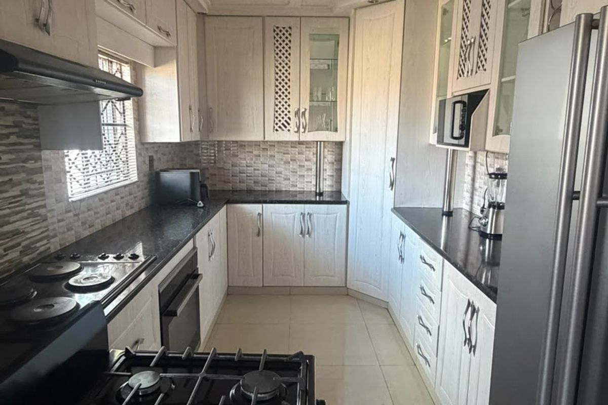 A functional kitchen featuring white cabinetry, dark granite countertops, a gas hob, built-in oven, and tiled backsplash with neutral floor tiles.