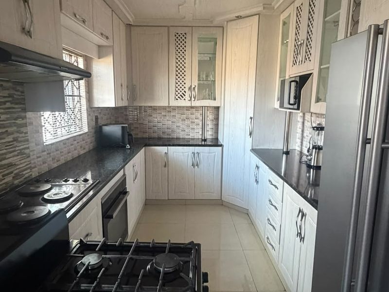A functional kitchen featuring white cabinetry, dark granite countertops, a gas hob, built-in oven, and tiled backsplash with neutral floor tiles.