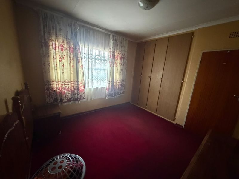 A bedroom featuring built-in wooden cupboards, security bars on the window, and red carpeting, presenting an opportunity for modernization.