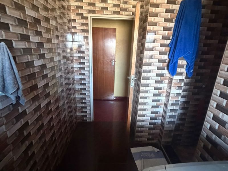 A functional laundry area featuring full-height decorative wall tiling and a standard internal door leading to an adjacent room.