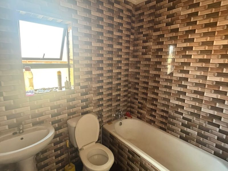 A functional bathroom featuring a pedestal basin, toilet, and bathtub with full-height decorative wall tiling and a top-hung window.