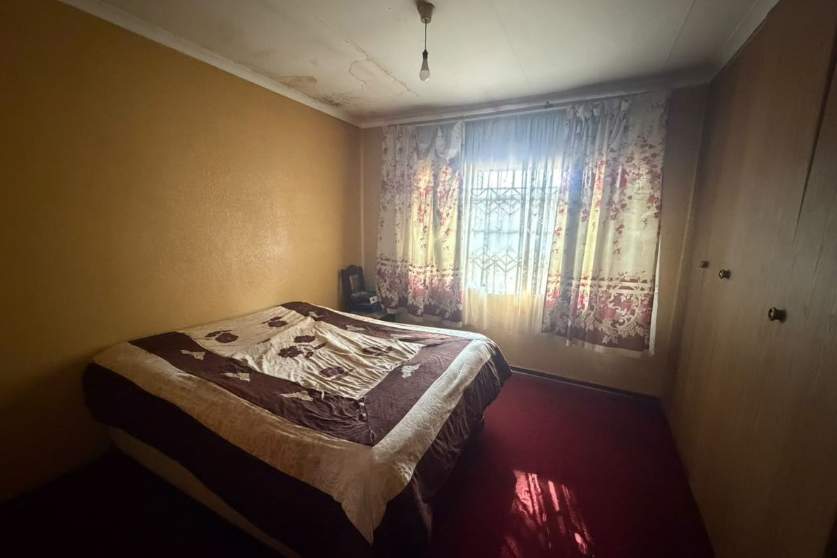 A bedroom featuring built-in cupboards and security bars on the window, showing signs of ceiling water damage and requiring cosmetic updates.
