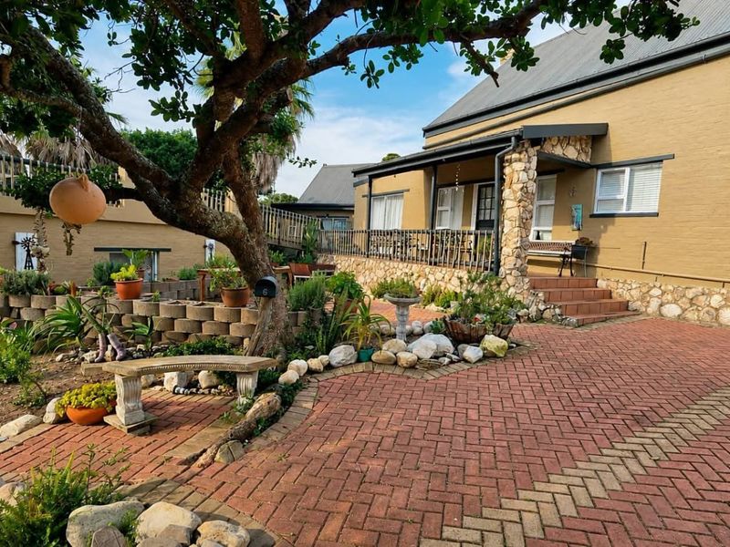Front exterior view of a house featuring a brick paved driveway, stone-clad accents, and a covered porch area with established garden landscaping.