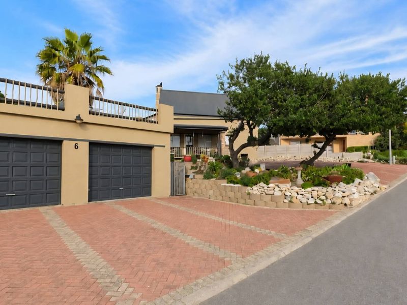 Front exterior view of the property featuring a double garage, paved driveway, and landscaped garden with a retaining wall.