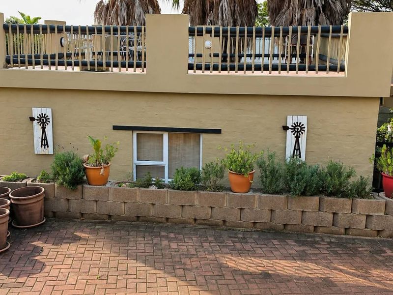 Rear exterior view featuring a paved driveway, a low retaining wall with garden beds, and an elevated balcony with a railing.