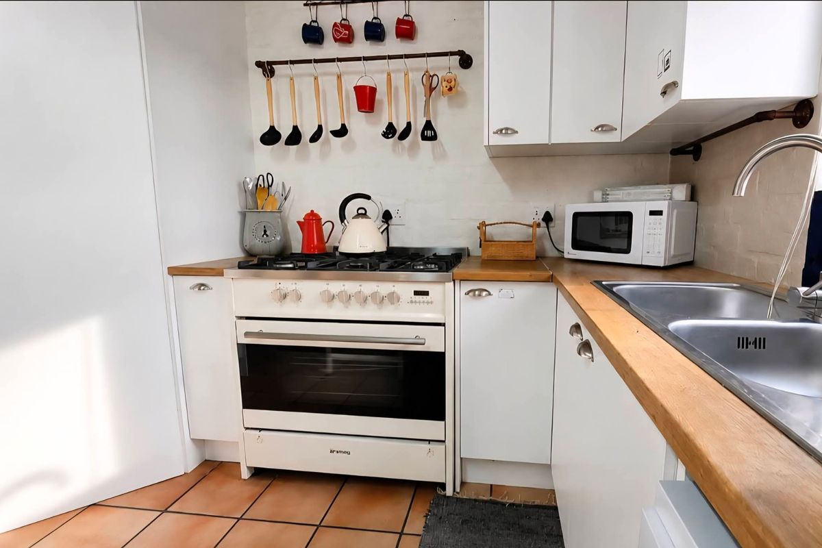 A functional kitchen featuring white cabinetry, wooden countertops, a gas stove with oven, and a stainless steel sink with a modern mixer tap.