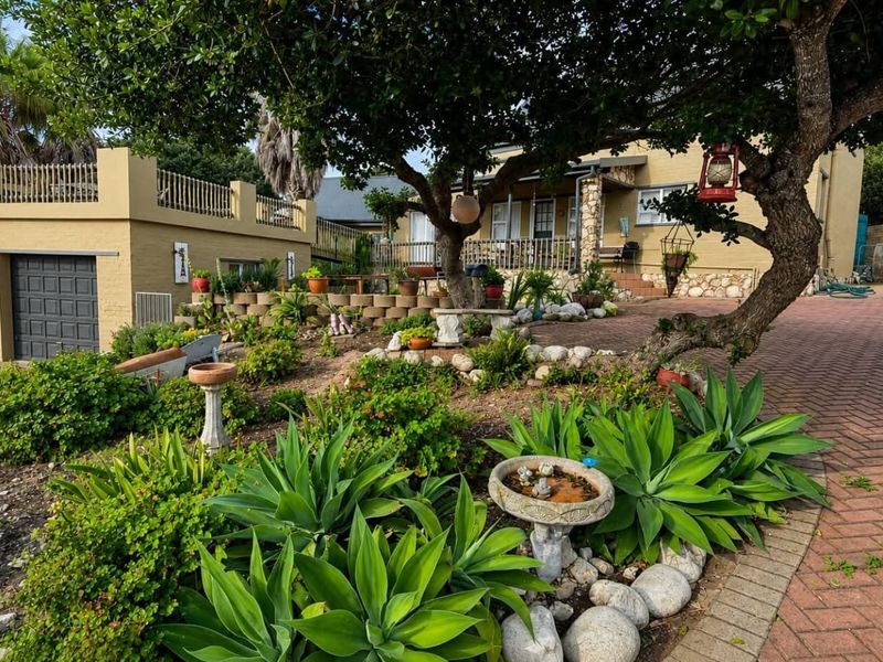 Front view of the property featuring a brick paved driveway, double garage, landscaped garden with stone retaining walls, and an elevated balcony.