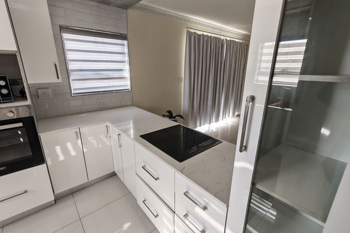 Modern kitchen featuring white glossy cabinetry, quartz countertops, integrated induction hob, built-in oven, and stylish subway tile backsplash with tiled flooring.