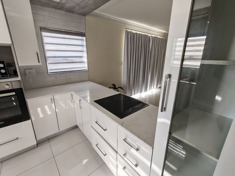 Modern kitchen featuring white glossy cabinetry, quartz countertops, integrated induction hob, built-in oven, and stylish subway tile backsplash with tiled flooring.