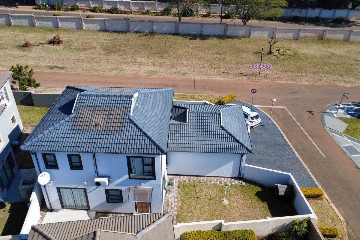 Aerial view of a residential property featuring a tiled roof with solar panels, a paved driveway, and a private garden area.