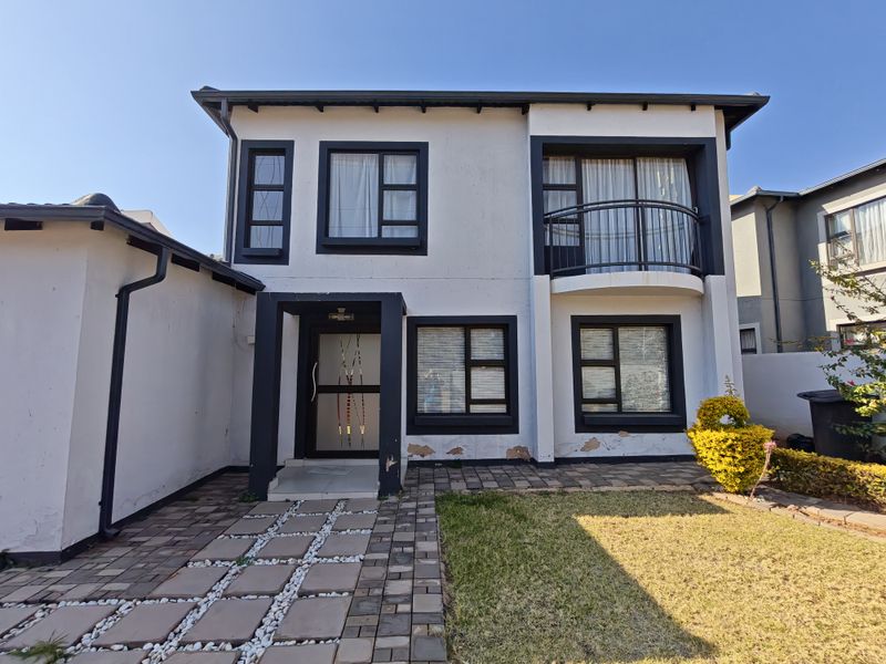 Front elevation of a two-story residential house featuring a paved walkway, balcony with metal railing, and modern aluminium window frames.