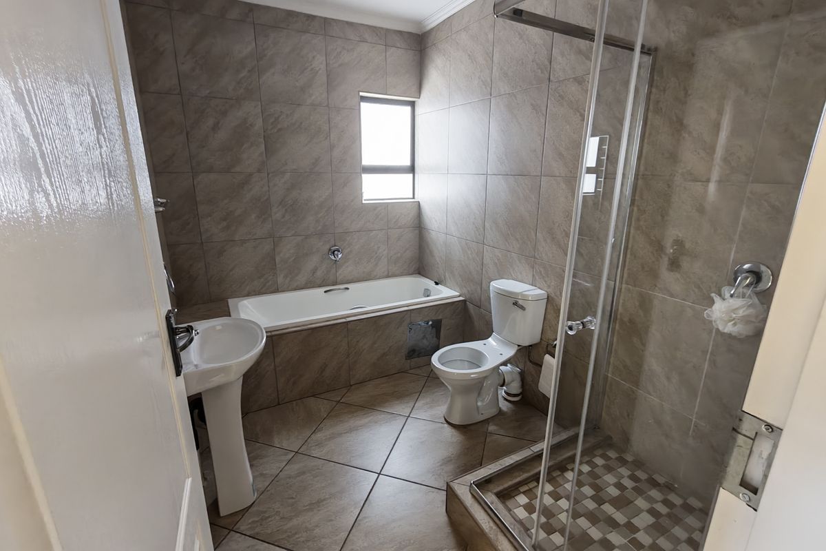 A functional bathroom featuring a pedestal basin, built-in bathtub, toilet, and a separate glass-enclosed shower with neutral floor-to-ceiling tiling.